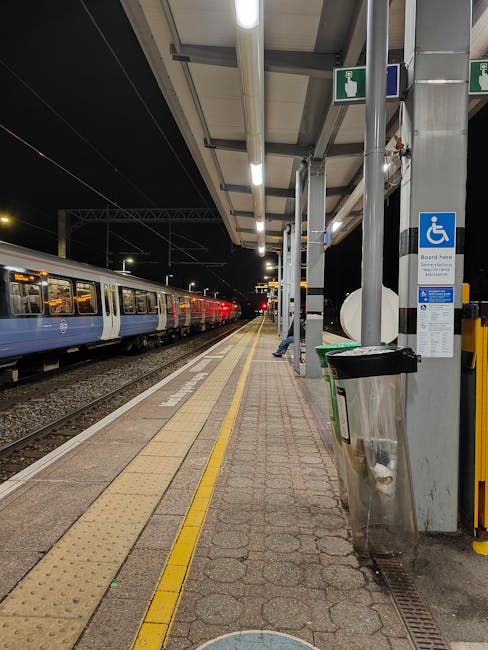 The image depicts a modern, streamlined train parked at a train station, with a sleek body finished in silver and accented with red highlights along the sides, including around the windows and door ar